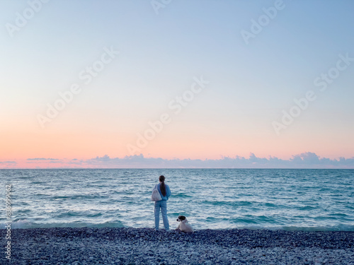 Silhouette of a girl and a dog on the beach at sunset. A summer evening. The concept of a family. A man and a pet. Sunrise. Copy space