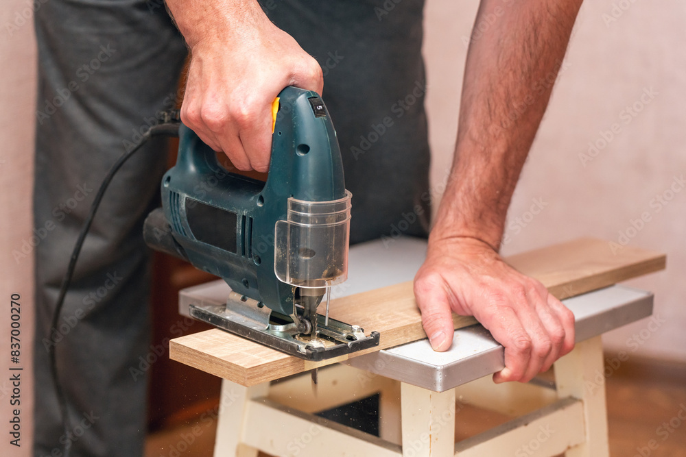 A worker cuts a board with a jigsaw A worker cuts a board with a jigsaw