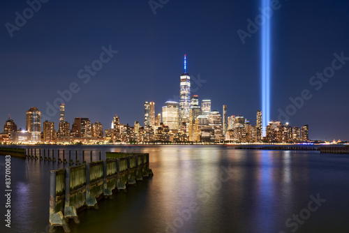 Lower Manhattan skyscrapers and September 11 Tribute in Light reflecting in Hudson River. Two vertical beams of light rise near World Trade Center in New York City