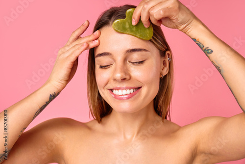 Closeup of a woman using a jade facial roller for skincare and selfcare on a pink background