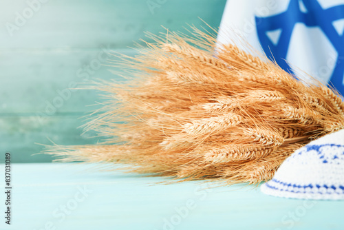Shavuot jewish background. Ripe bouquet of wheat with blue ribbon against the background of Israeli flag and old wooden wall with sun rays. Background for Shavuot celebration. Mock up.