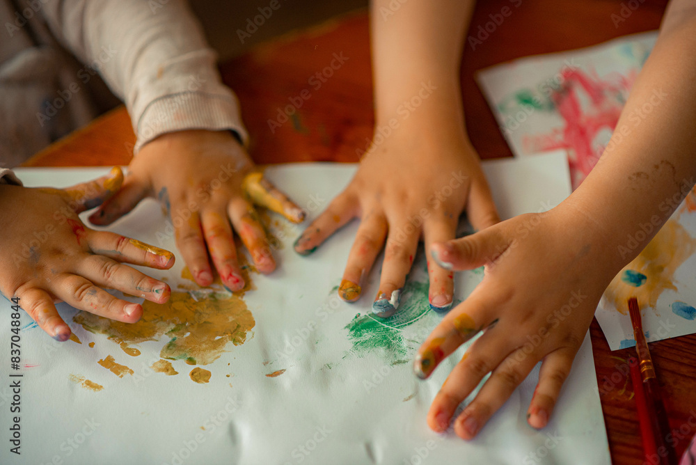 small children draw different doodles on a piece of paper with paints, their palms are all covered in paints small children draw different doodles on a piece of paper with paints, their palms are all covered in paints