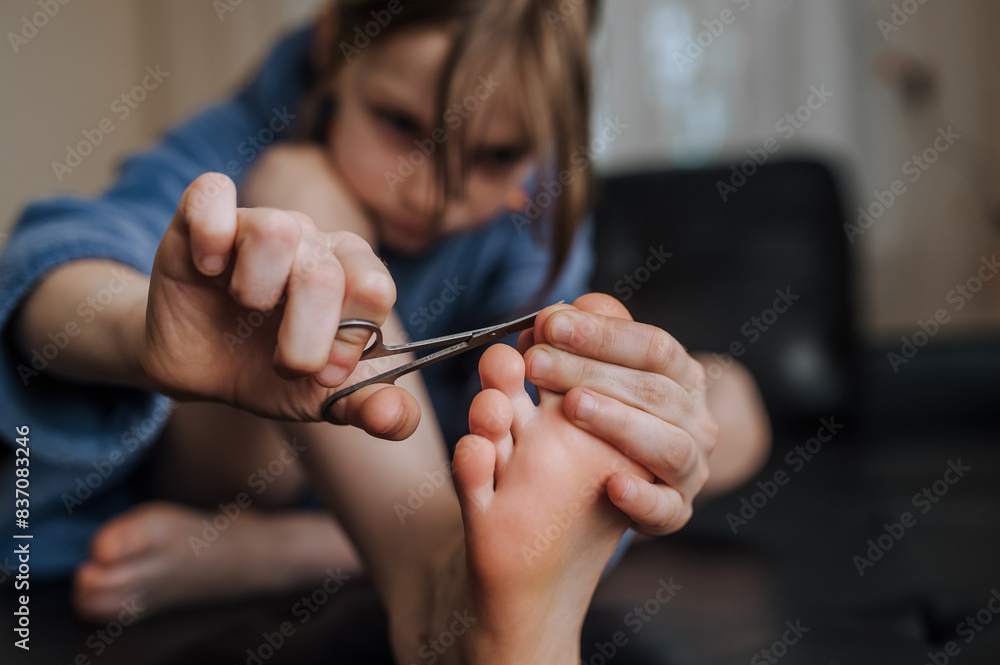 Φωτογραφία A girl, a child caring for health, sits in the room on the sofa, independently cutting her toenails with manicure scissors