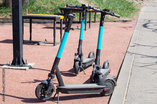 Parked electric scooters ready for rental in a park, with fitness equipment visible in the background.