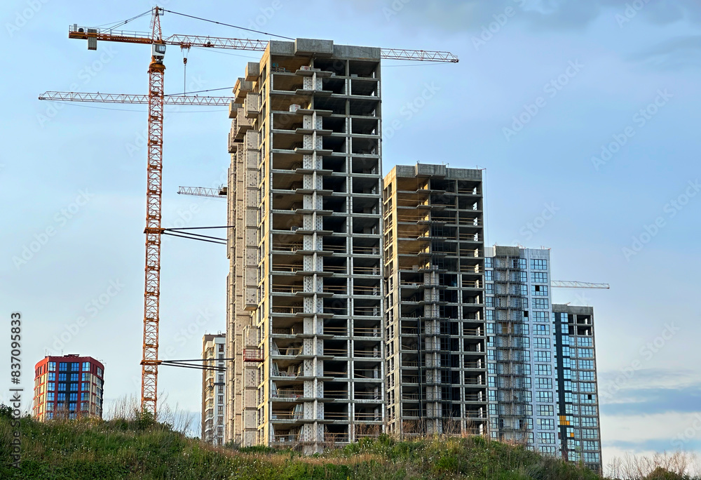 Fototapeta premium Construction site with buildings under construction. Tower cranes in action. Crane during formworks of house. Multi Storey Residential Buildings construction. Tower crane on Housing renovation.