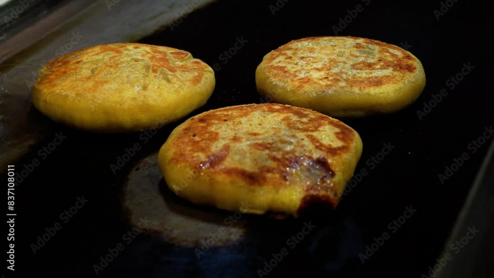 A metal spatula flips three golden brown gamchi or korean potato bread on a grill. A metal spatula flips three golden brown gamchi or korean potato bread on a grill.