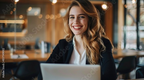 A woman is sitting at a table with a laptop in front of her. She is smiling and she is happy