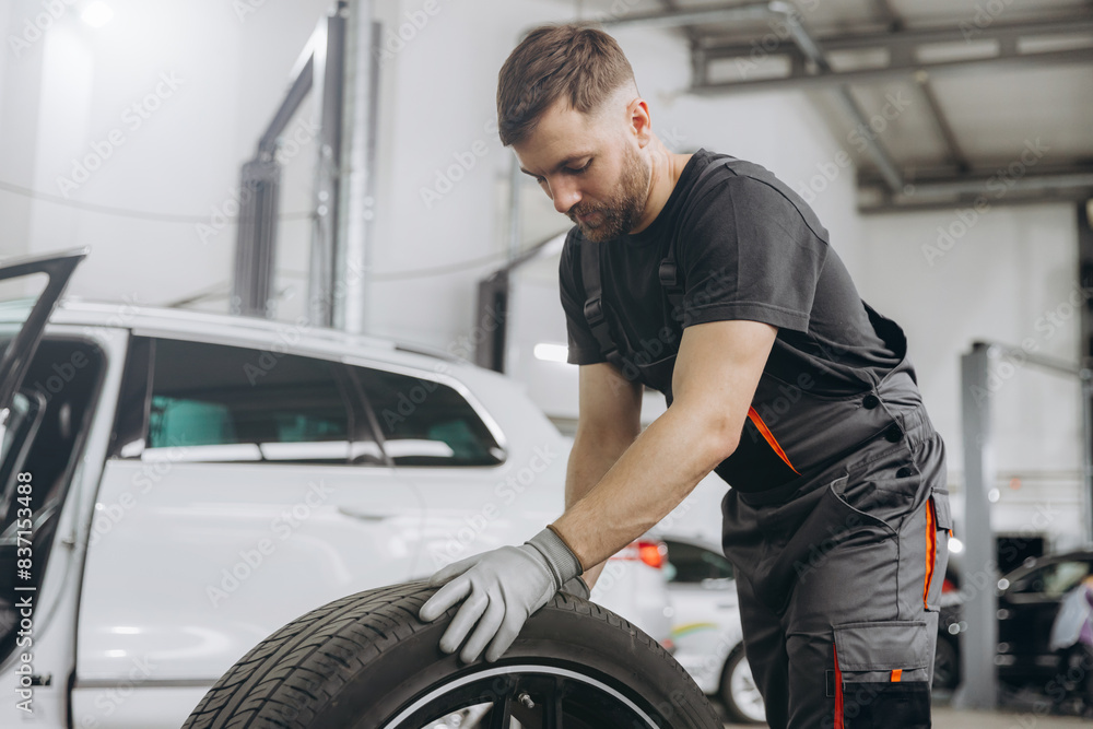 Happy Car Mechanic holding a tire at the repair garage. Replacement of winter and summer tires Happy Car Mechanic holding a tire at the repair garage. Replacement of winter and summer tires