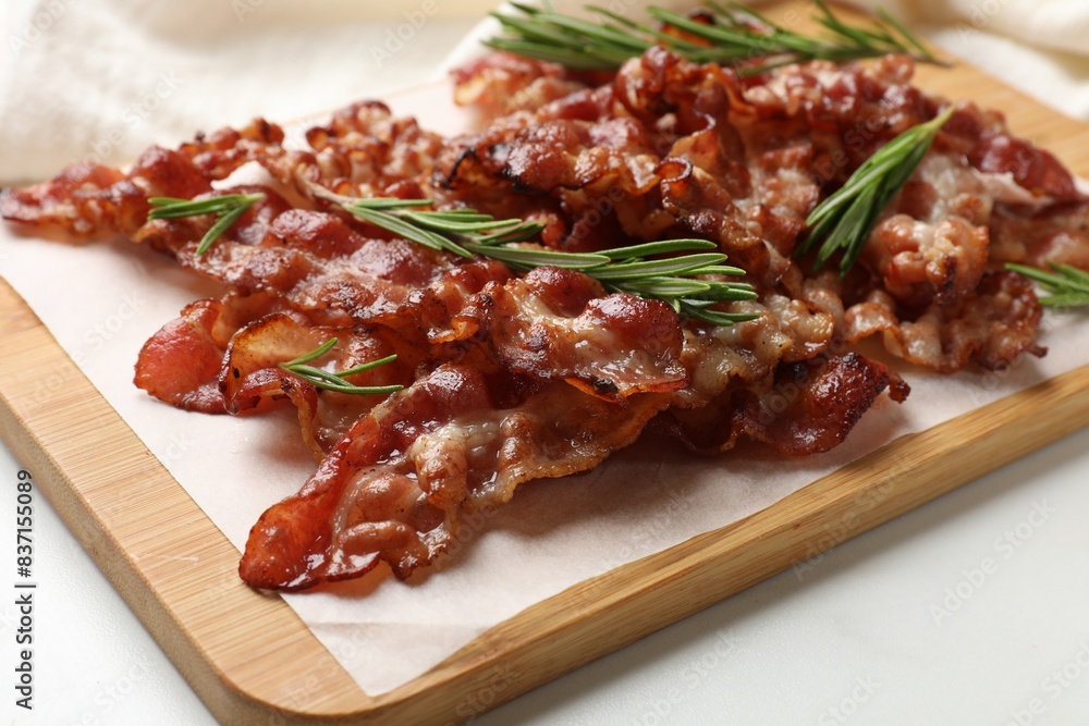 Slices of tasty fried bacon with rosemary on white table, closeup Slices of tasty fried bacon with rosemary on white table, closeup