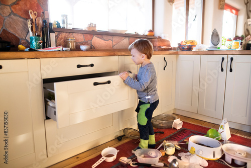 Tableau sur toile Little boy is taking kitchen utensils out of the drawers, making a mess in the kitchen