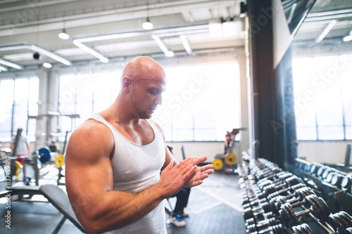 Strong man exercising in gym, looking at chalk on his palms. Routine workout for physical and mental health. © Halfpoint