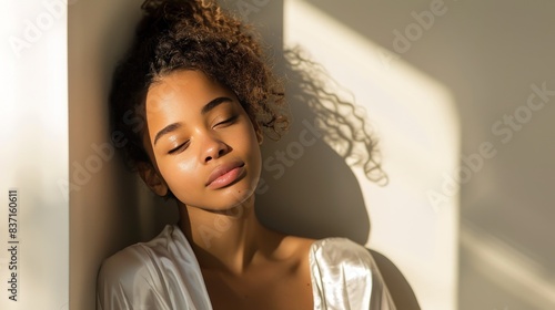 belle femme afro-américaine sensuelle en vêtements de soie blanche profitant de la lumière du matin sur fond blanc avec des ombres photo