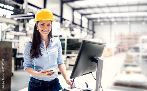 Female project manager standing by computrer in modern industrial factory. Manufacturing facility with robotics, robotic arms and automation. Storing products and materials in warehouse. photo