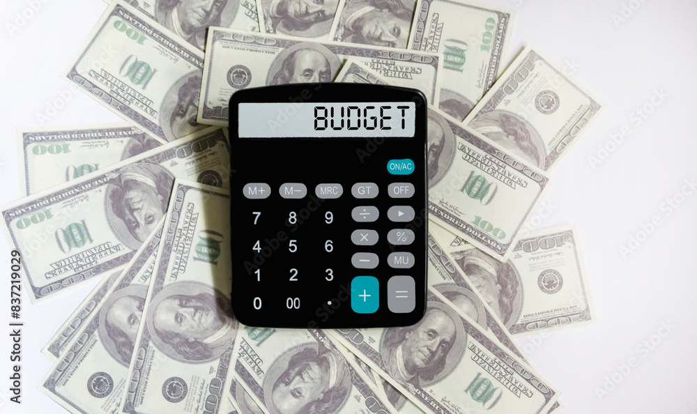 Calculator with the word BUDGET on the display. One hundred dollar bills lie on a white background. Conceptual photo. Calculator with the word BUDGET on the display. One hundred dollar bills lie on a white background. Conceptual photo.