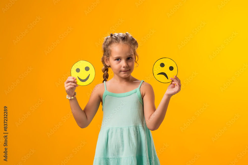 Kid girl holding sad and happy emoticons in hands. Mental health, psychology and children's emotions concept Kid girl holding sad and happy emoticons in hands. Mental health, psychology and children's emotions concept