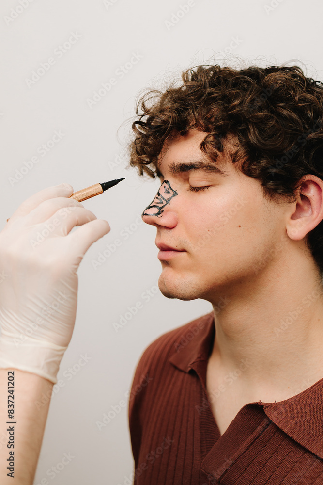 Obraz premium Process of drawing markup on male nose before rhinoplasty and septoplasty surgery. ENT doctor preparing patient for rhinoplasty surgery that changes the shape of the nose.