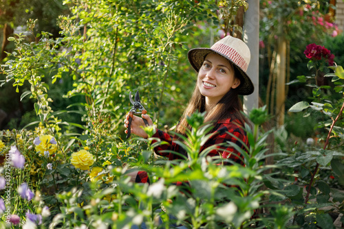 smiling young woman gardener trimming flowers with secateurs