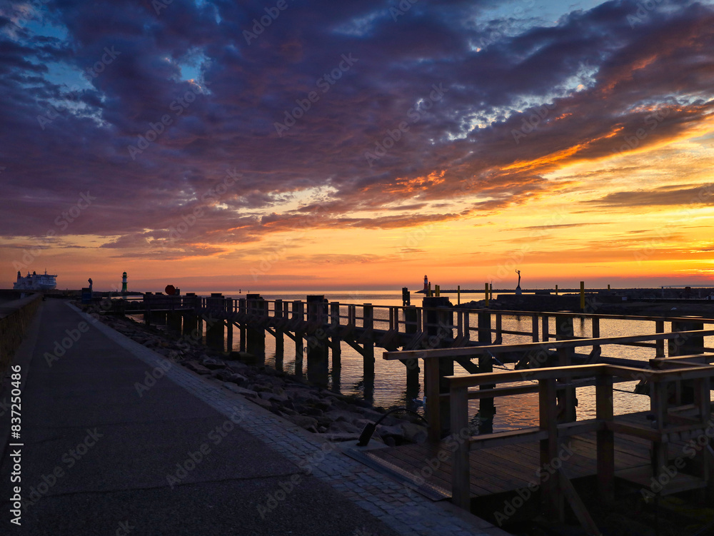 Obraz premium Blick von der Westmole auf die Hafeneinfahrt bei Sonnenaufgang, hölzerne Anlegesteg-Konstruktionen im Morgenrot, maritime Küstenlandschaft, Warnemünde, Rostock, Mecklenburg-Vorpommern, Deutschland