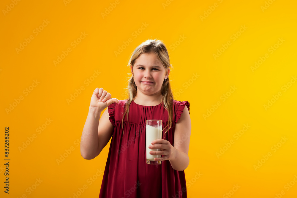 Kid girl with dairy allergy holding glass of milk and showing thumb down gesture on yellow background. Lactose intolerance concept Kid girl with dairy allergy holding glass of milk and showing thumb down gesture on yellow background. Lactose intolerance concept