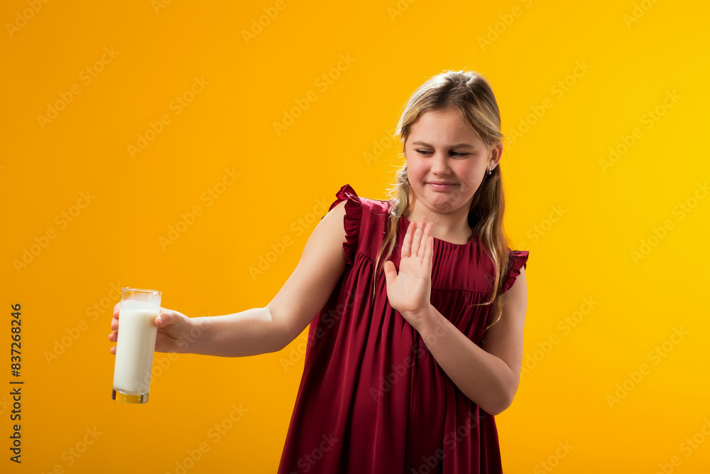 Naklejka premium Kid girl with dairy allergy showing stop gesture front glass of milk on yellow background. Lactose intolerance concept