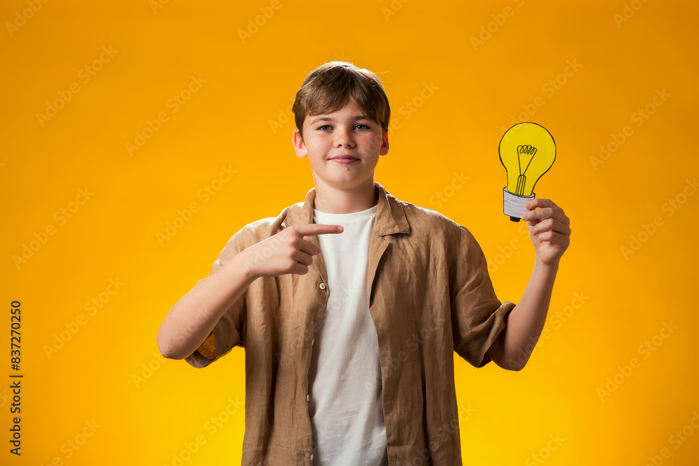 Boy holding paper bulb and pointing finger at it. Success, motivation, winner, genius, idea concept Boy holding paper bulb and pointing finger at it. Success, motivation, winner, genius, idea concept