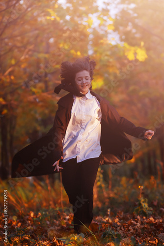girl in black raincoat runs along the alley of city park the background of autumn maples, autumn toning, autumn background, selective focus