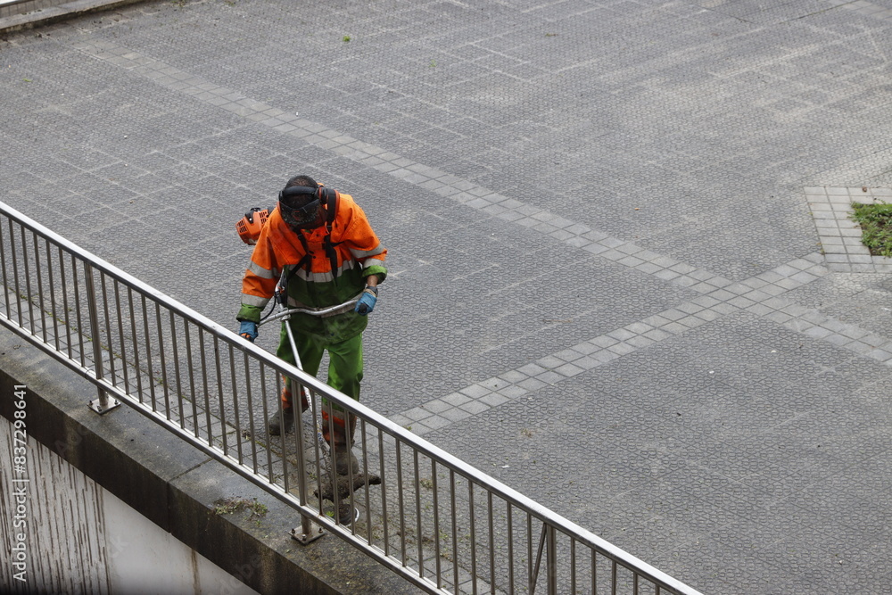 Man cutting the grass in the street with a brush cutter wearing a mask and protective equipment Man cutting the grass in the street with a brush cutter wearing a mask and protective equipment