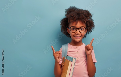 Happy Young Girl With Backpack Pointing Up Against A Blue Background
