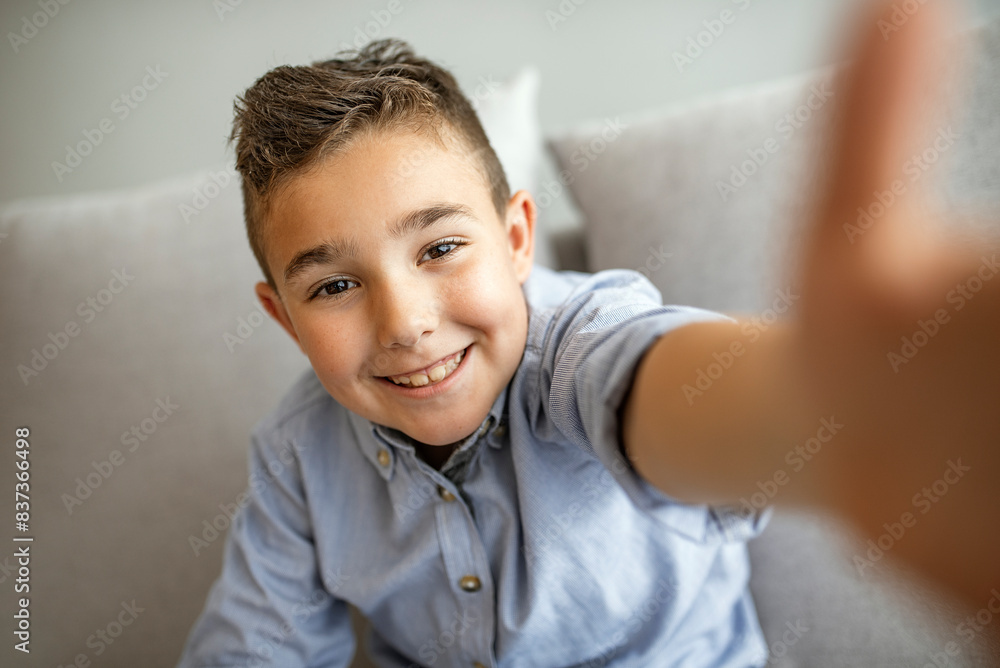Cute little boy taking selfie on light background. Happy little boy with healthy teeth taking selfie. Photo of boy takes selfie with smart phone indoors. Boy takes selfie Cute little boy taking selfie on light background. Happy little boy with healthy teeth taking selfie. Photo of boy takes selfie with smart phone indoors. Boy takes selfie