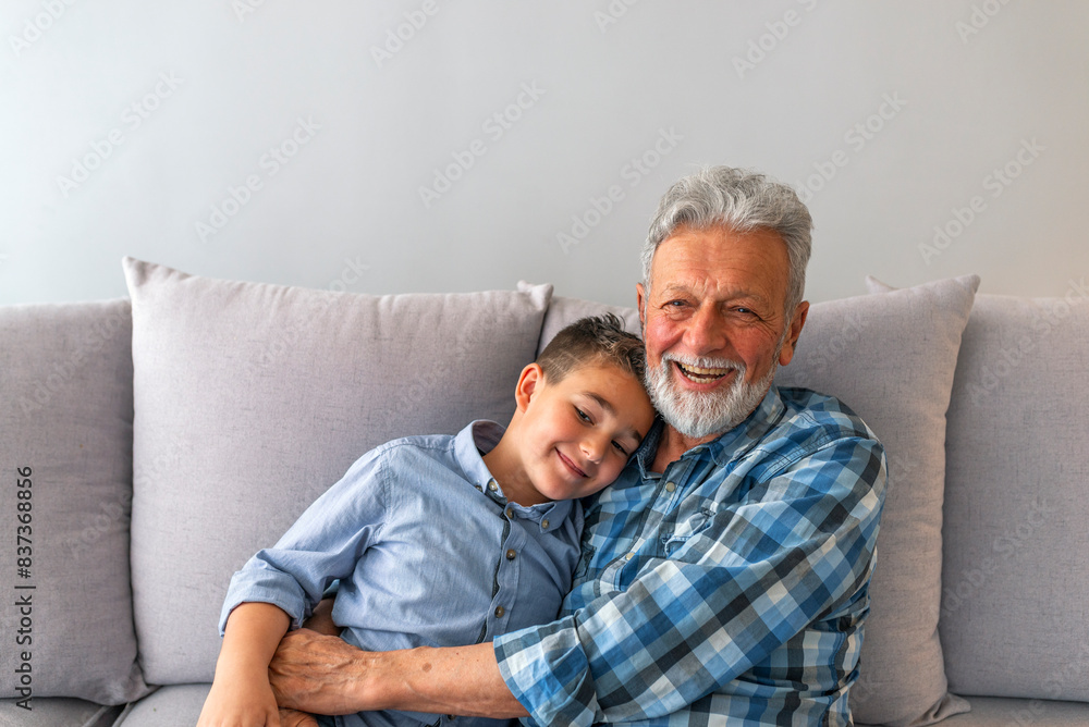 Grandpa and grandson are playing, hugging, looking at camera and smiling while resting together at home. Happy grandfather sit on couch enjoy spending time with preschooler grandson at home Grandpa and grandson are playing, hugging, looking at camera and smiling while resting together at home. Happy grandfather sit on couch enjoy spending time with preschooler grandson at home