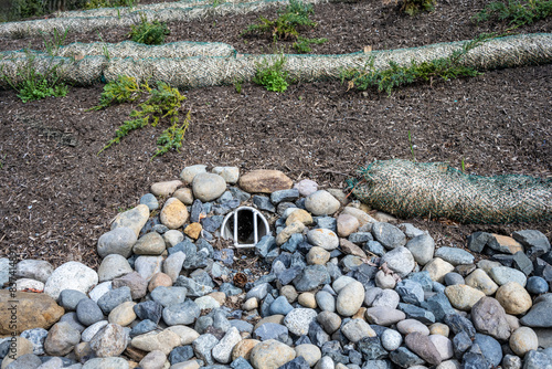 New installation of storm water flood management, round outflow pipe leading to a flow of river rock leading to a large storm drain, straw wattle preventing new ground bark from reaching drain
 photo