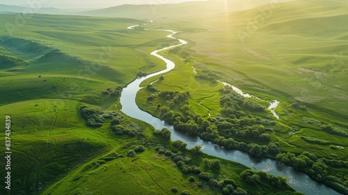 A drone shot of a meandering river through a lush green valley at sunrise