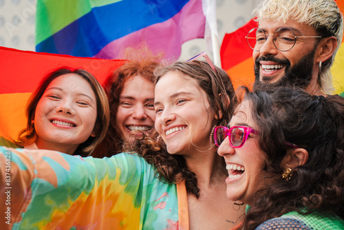 Close up portrait of a group of LGBT poeple having fun celebrating the gay pride day with a rainbow flag. Young adult LGTB friends on a sexual rights party smiling with freedom and courage expression photo