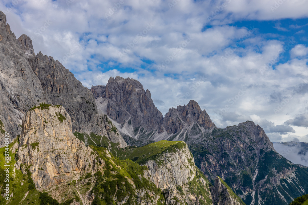 Dolomiti Alps beautiful mountain landscape. Rocky tower alpine summits in the Dolomites. Summer mountain scenic view on the hiking trekking path in the green mountain valley and blue sky with clouds Dolomiti Alps beautiful mountain landscape. Rocky tower alpine summits in the Dolomites. Summer mountain scenic view on the hiking trekking path in the green mountain valley and blue sky with clouds