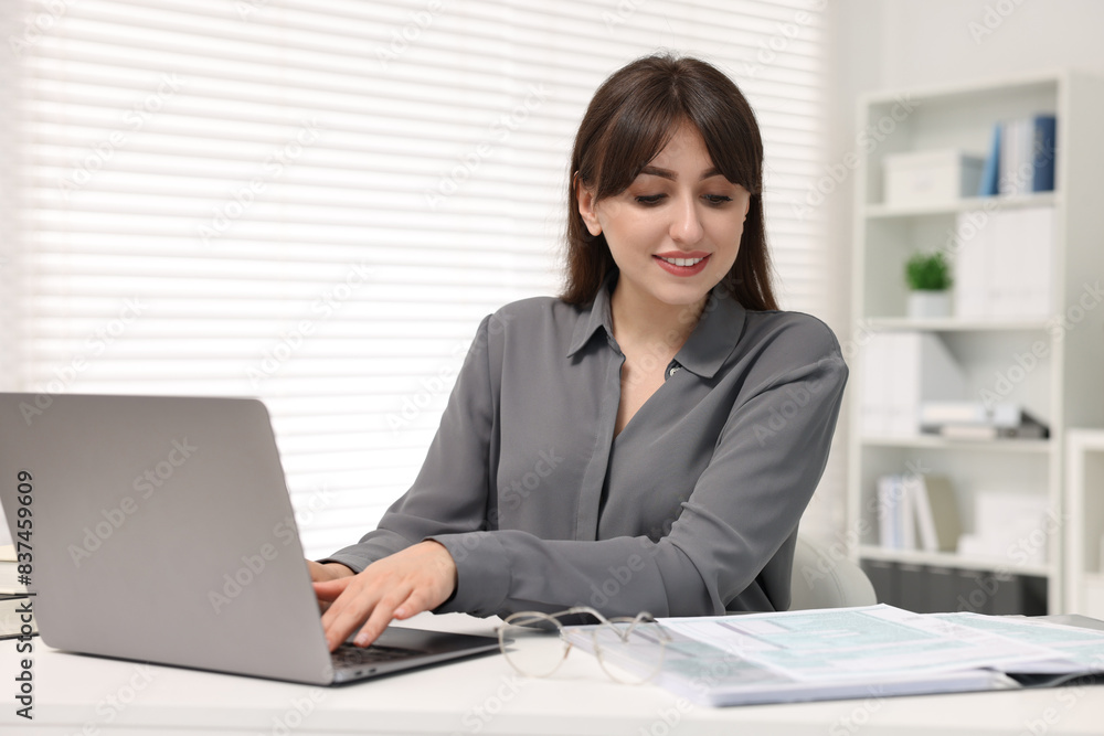 Smiling secretary working with laptop at table in office Smiling secretary working with laptop at table in office