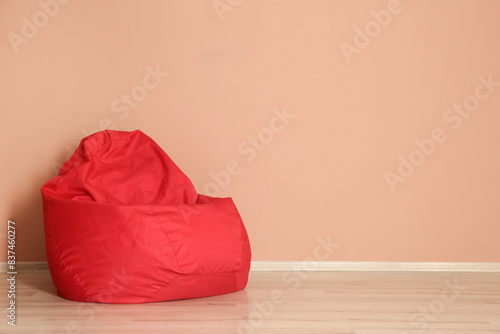 Red bean bag chair on floor near beige wall indoors, space for text photo