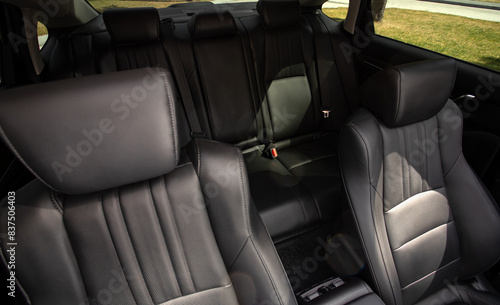Close-up  leather  black     rear seat made of  in the background passenger seats with seat belts. Luxury car interior © Виталий Сова