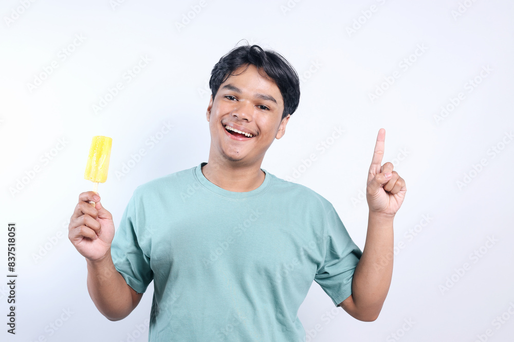 Happy Young Asian Man Pointing To Upwards While Holding Ice Cream Stick Isolated On White Background Happy Young Asian Man Pointing To Upwards While Holding Ice Cream Stick Isolated On White Background