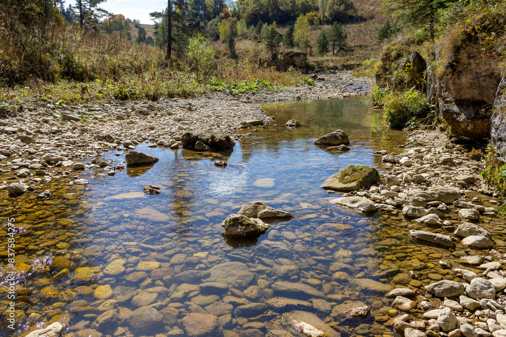 Shallow riverbed with a rocky bottom , unhurried flow of water, autumn walks in nature Shallow riverbed with a rocky bottom , unhurried flow of water, autumn walks in nature