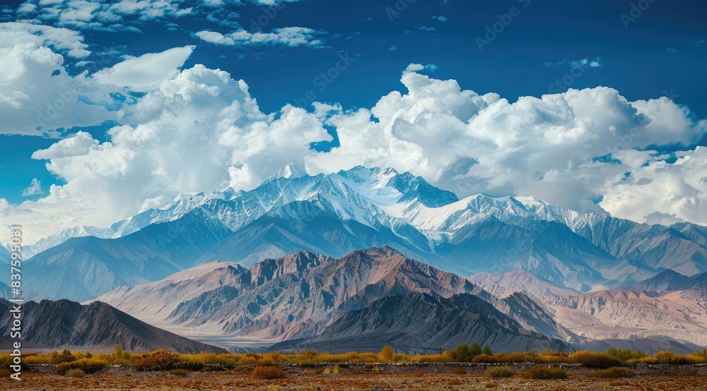 Fototapeta premium Majestic snow-capped mountain range under a blue sky with clouds