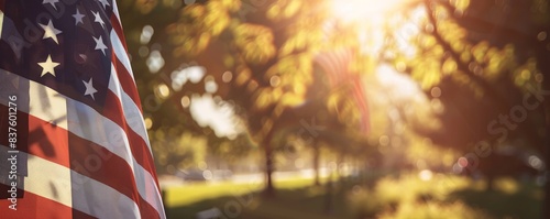 The photo shows an American flag waving in the wind with a blurred background of trees and sunlight.