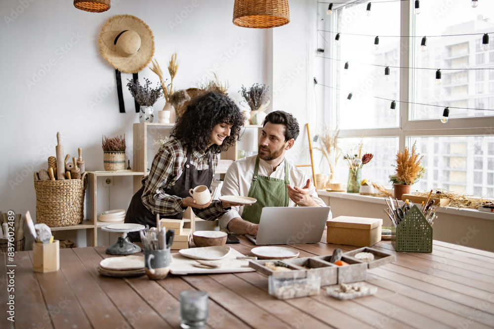 © sofiko14 - Portrait of mature man and young curly woman creating online catalogue of available goods at decor store. Two workers holding original ceramic products, using laptop during working at shop. © sofiko14 - Portrait of mature man and young curly woman creating online catalogue of available goods at decor store. Two workers holding original ceramic products, using laptop during working at shop.