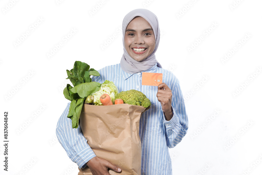 Young woman wear casual clothes hold brown paper bag with vegetable products mock up of credit bank card isolated on white background studio portrait Young woman wear casual clothes hold brown paper bag with vegetable products mock up of credit bank card isolated on white background studio portrait