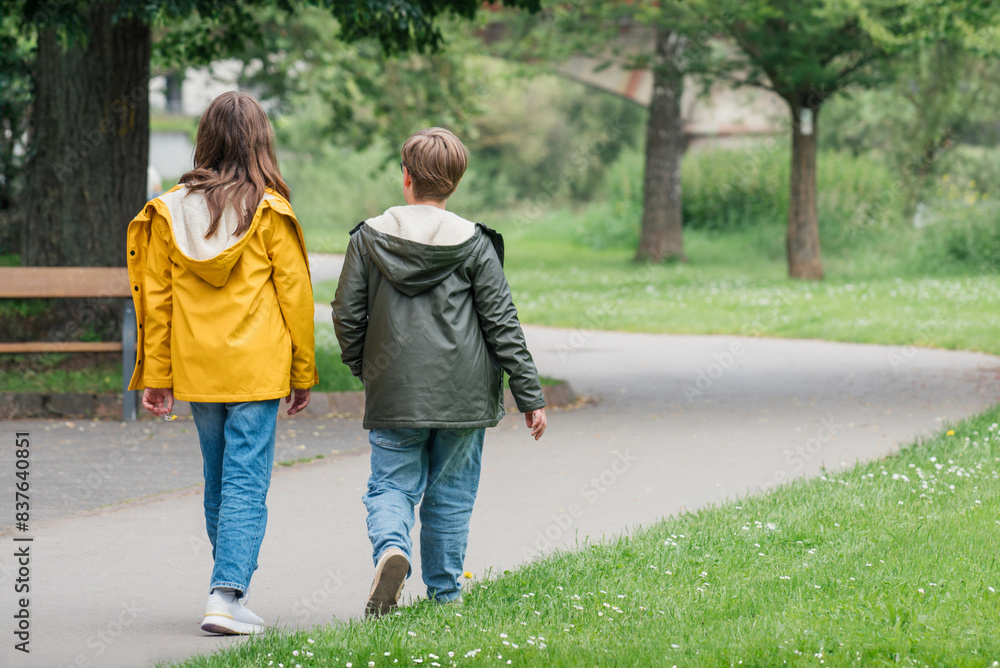 A teenage girl and boy are walking in a spring park. Wearing lightweight weather jackets A teenage girl and boy are walking in a spring park. Wearing lightweight weather jackets