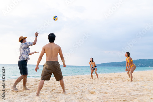 Group of Happy Asian man and woman enjoy and fun outdoor lifestyle travel at the sea on summer holiday vacation. People friends playing beach volleyball together on tropical island beach at sunset.