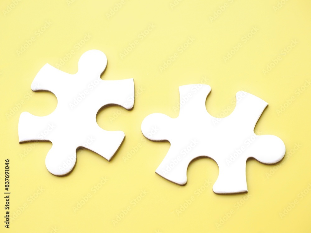 Two complementary white jigsaw puzzle pieces on a yellow background, symbolizing association, connection, or interdependence. Copy space to add text Two complementary white jigsaw puzzle pieces on a yellow background, symbolizing association, connection, or interdependence. Copy space to add text
