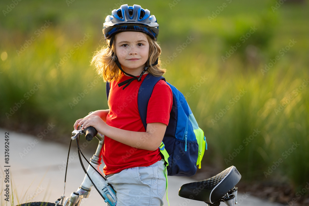Naklejka premium Little kid boy ride a bike in the park. Kid cycling on bicycle. Happy smiling child in helmet riding a bike. Boy start to ride a bicycle. Sporty kid bike riding on bikeway. Kids bike.