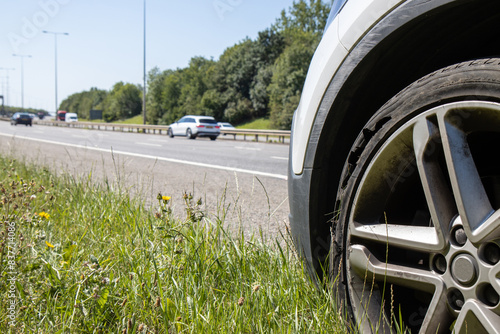 A car with a flat tyre after a large blow out on the highway showing a large slit in the tyre at the side of the M25 motorway in London in the UK