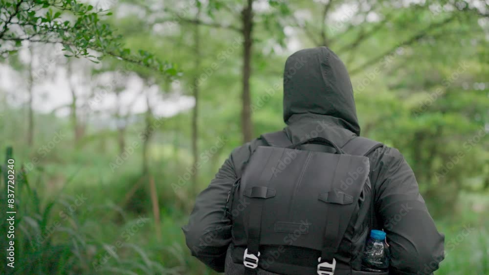 Slow motion image of a man wearing a green hooded jacket. A backpack is available for summer walks along the forest trails. Slow motion image of a man wearing a green hooded jacket. A backpack is available for summer walks along the forest trails.
