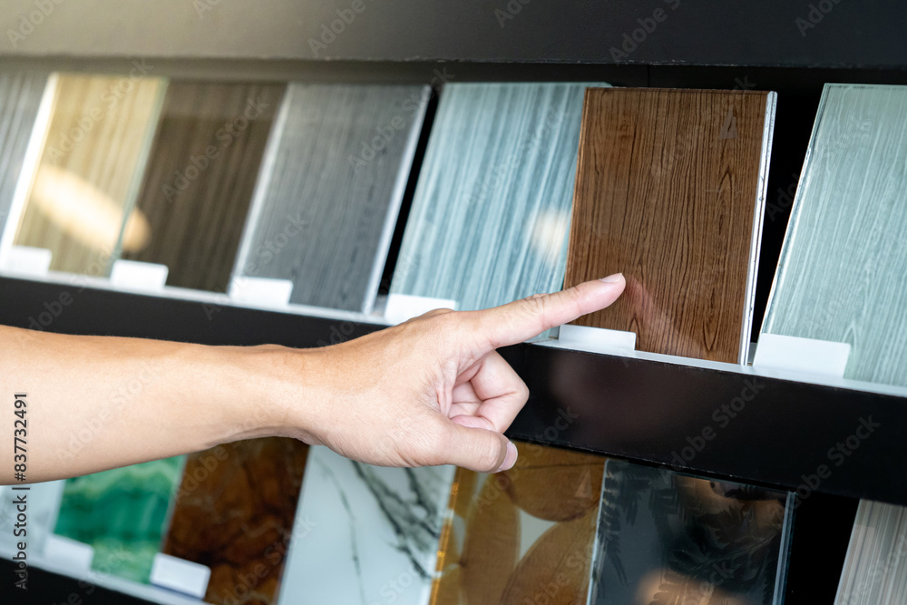 Obraz premium Architect hand choosing and pointing at brown tile material samples on the ceramic collection shelf display in the material library. Designer working for interior architecture project